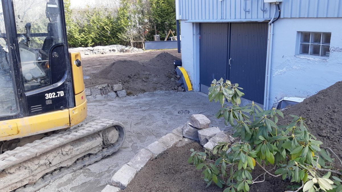 Pieni kaivuri valkoisen omakotitalon kulmalla