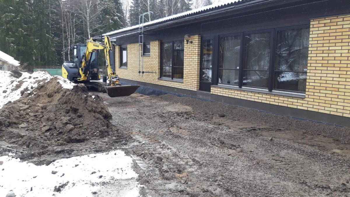 Pieni kaivuri keltaisen tillitalon vieressä